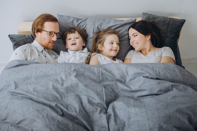 Los padres jóvenes con niños se divierten en la cama los fines de semana.