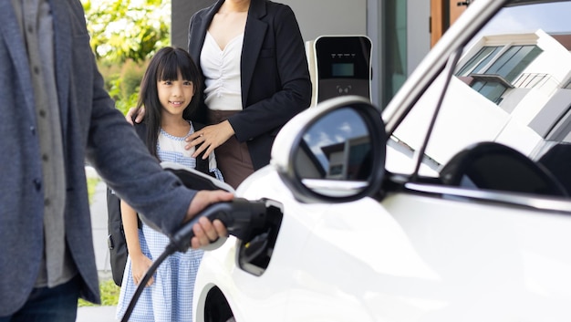 Padres jóvenes progresistas e hija que viven en una casa con un auto eléctrico