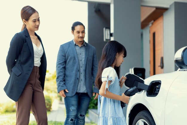 Padres jóvenes progresistas e hija que viven en una casa con un auto eléctrico