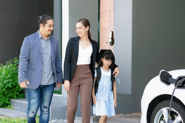 Padres jóvenes progresistas e hija que viven en una casa con un auto eléctrico