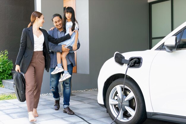 Padres jóvenes progresistas e hija que viven en una casa con un auto eléctrico