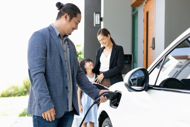 Padres jóvenes progresistas e hija que viven en una casa con un auto eléctrico