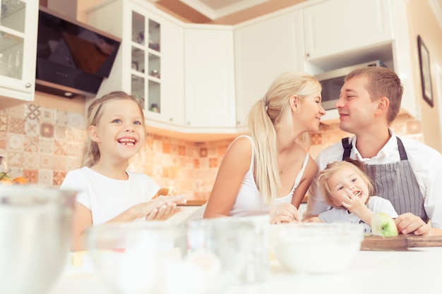 Los padres jóvenes y sus dos niñas hermosas y lindas niñas cocinando y desayunando