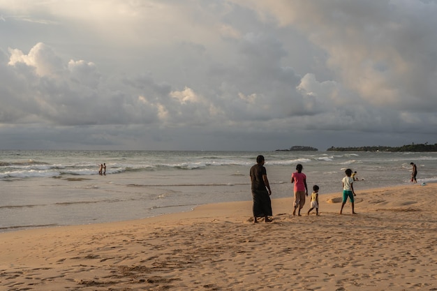 Los padres jóvenes y sus hijos caminan por la playa.