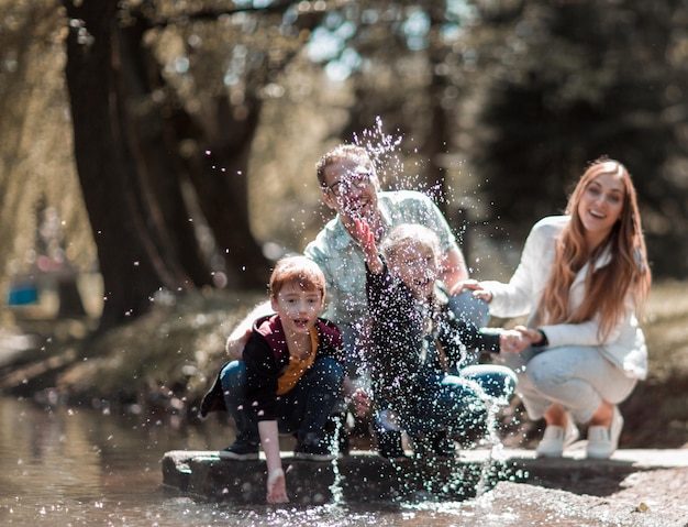 Los padres juegan con los niños cerca del lago en el parque de la ciudad el concepto de entretenimiento familiar