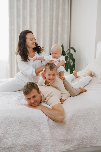 Padres jugando con niños en la cama en un acogedor piso blanco