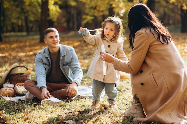 Padres jugando con su hija en pompas de jabón en el parque de otoño