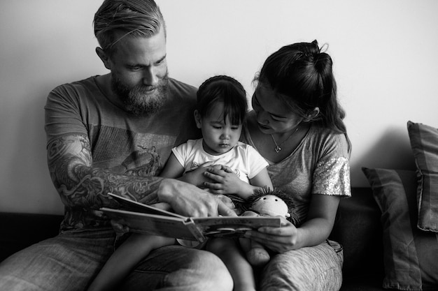 Foto padres leyendo un libro a su pequeña hija.