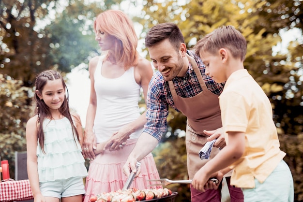 Los padres con niños hacen barbacoa.