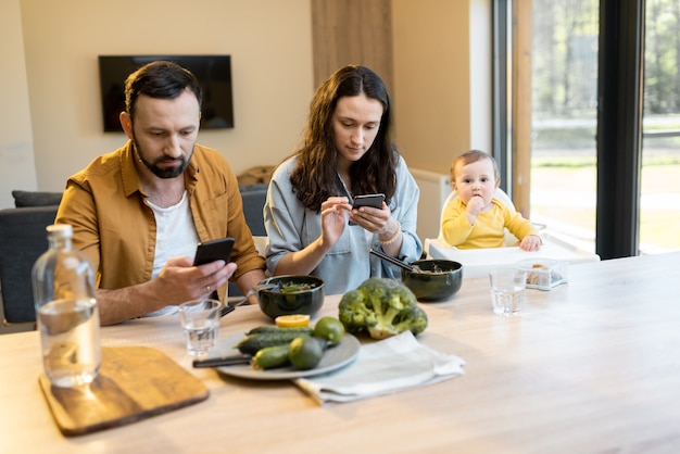 Los padres ocupados en sus teléfonos durante un almuerzo con su hijo