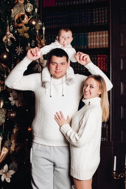 Padres posando con bebé. Árbol de navidad detrás.