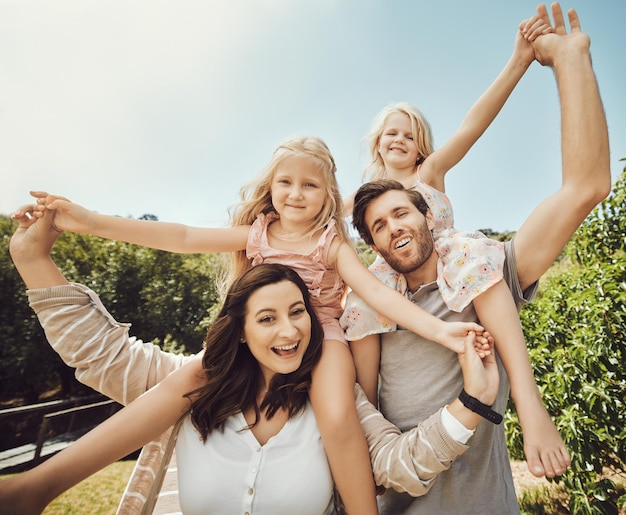 Los padres retratados llevan a las niñas y en la naturaleza tiempo de calidad y vinculación en la felicidad del fin de semana o juguetón Amor madre y padre con hijas en el hombro al aire libre o familia en descanso relajarse o amar