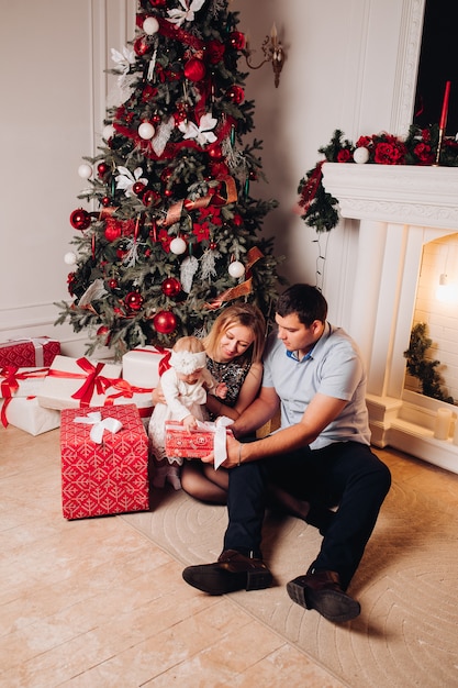 Padres sentados en el piso con el niño cerca del árbol de Navidad.