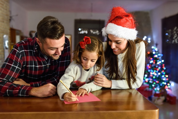 Foto padres con su hija escribiendo la carta a papa noel