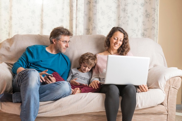 Foto padres con su hijo usando una computadora portátil en el sofá en casa