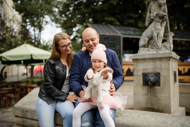 Los padres y su pequeña hija están sentados en la antigua fuente de la ciudad.