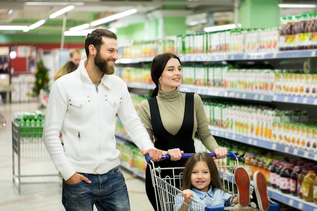 Los padres y su pequeña hija sonríen mientras eligen comida en el supermercado