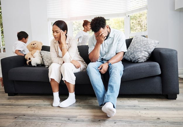 Foto padres tristes, infelices y estresados sentados en un sofá cerca de sus hijos en casa después de una discusión frustrados, cansados y molestos, mamá y papá están enojados con los niños hiperactivos, ruidosos y traviesos