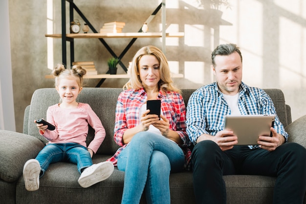 Foto padres usando tableta digital y teléfono móvil mientras su hija mira televisión.