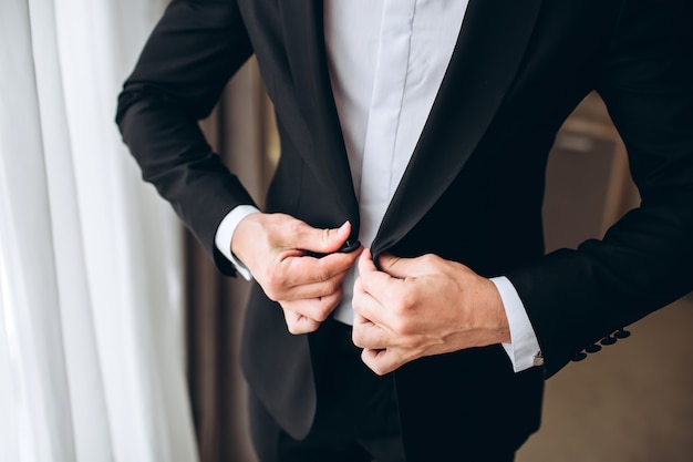 Padrinos de boda con estilo que ayudan al novio feliz que se prepara en la mañana para la ceremonia de boda. Hombre de lujo en traje en la habitación. día de la boda.