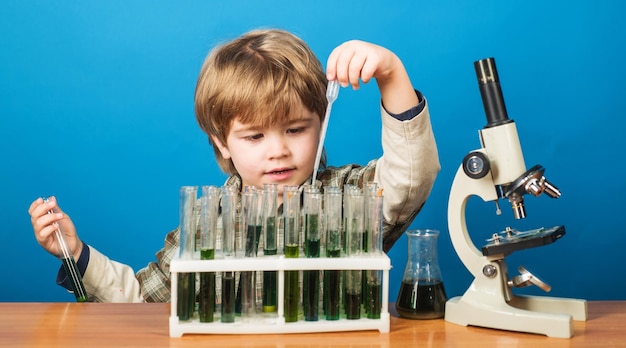 Pädagogischer Experimentierjunge mit Reagenzgläsern und Mikroskop im Schulklassenzimmer-Wissenstagkind