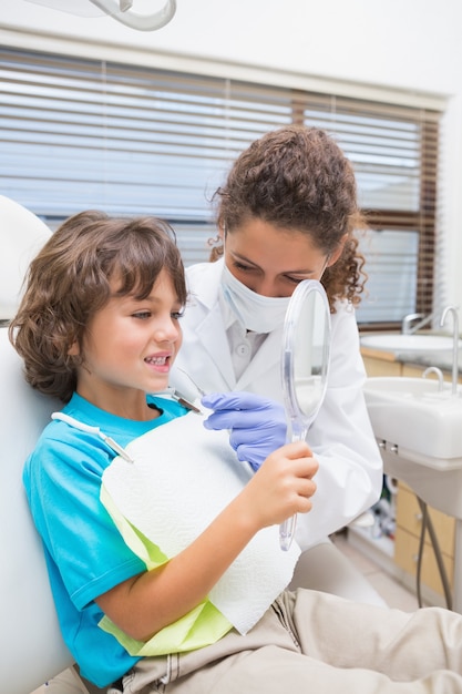 Pädiatrischer Zahnarzt, der kleinem Jungen seine Zähne im Spiegel zeigt