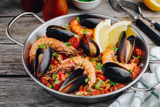 Paella española de marisco con mejillones, gambas y chorizo en una sartén tradicional sobre fondo de madera