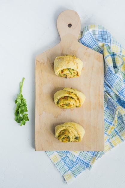 Pães caseiros com alho, salsa verde e pimentão em um guardanapo e tábua de madeira branca.