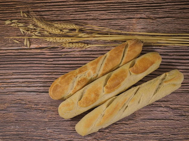 Foto pães caseiros de estilo francês em fundo de madeira e com decoração de trigo e aveia