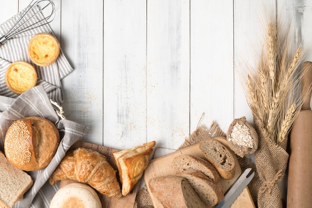 Pães caseiros ou pão, croissant e ingredientes de padaria em fundo branco de madeira, café da manhã co de alimentos