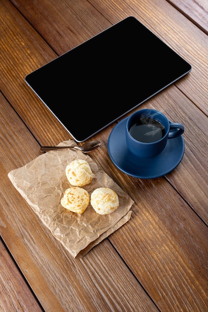 Pães de queijo brasileiros ao lado da colher de cobre da xícara de café e tabletvertical