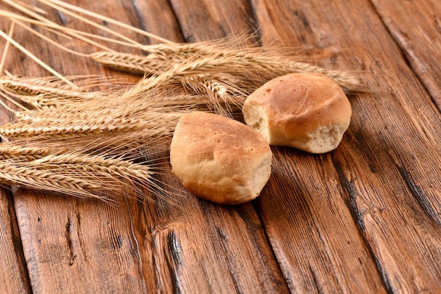 Pães recém-assados e espigas de trigo em uma mesa de madeira