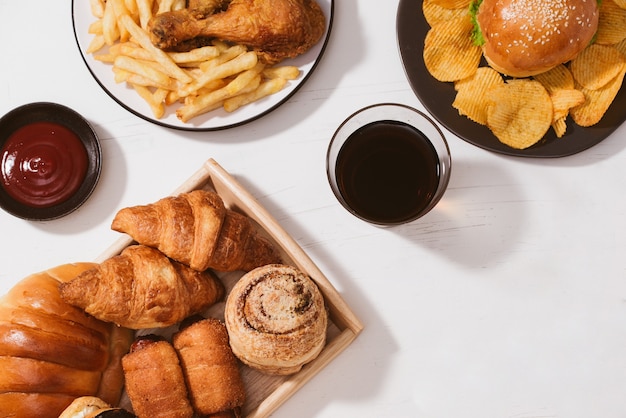 Pães recém-assados, hambúrguer grande, frango crocante frito e batatas fritas na mesa branca - conceito de comida não saudável