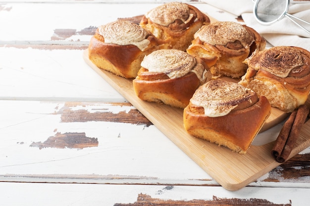 Pãezinhos de canela Kanelbulle com creme de manteiga em uma mesa de madeira rústica. Pastelaria fresca caseira.