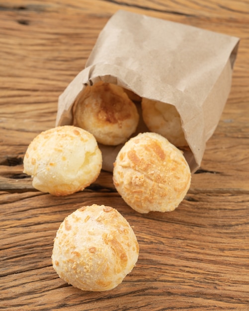 Pãezinhos de queijo brasileiro típico em um saco de papel sobre a mesa de madeira.