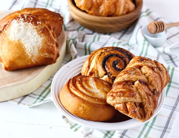 Pãezinhos doces caseiros recém-assados com sementes de papoula e mel na mesa, no pires a bordo e na tigela de madeira