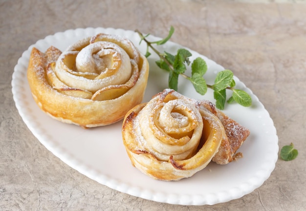 Pãezinhos folhados em forma de rosas com uma maçã e um raminho de hortelã em um prato oval branco