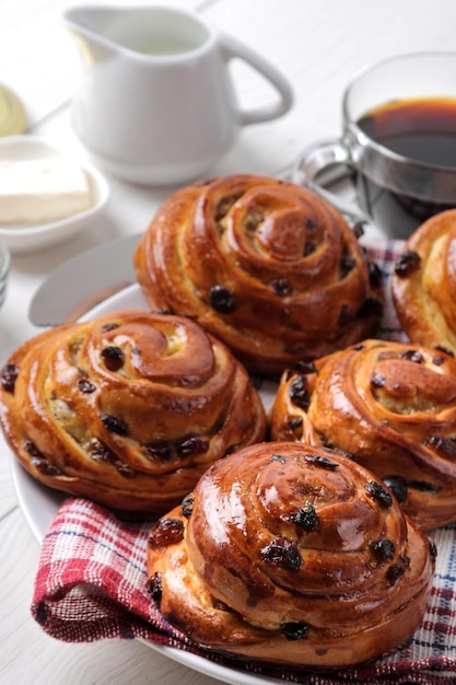 Pãezinhos saborosos com passas e café com leite em um café da manhã fresco de padaria de fundo branco de madeira