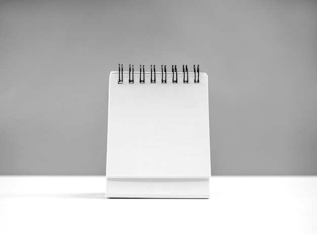 Página en blanco de calendario en espiral de escritorio para el organizador concepto para planificar y recordatorio de pie en la mesa blanca sobre fondo gris Mock up pequeña mesa calendario papel vista frontal plantilla foto para el diseño