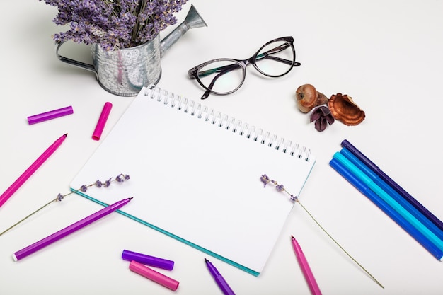 Página en blanco de la libreta espiral en mesa blanca. Lápiz de crayón y pluma plana foto puesta. Página de cuaderno de bocetos vacía en la vista superior de la mesa.