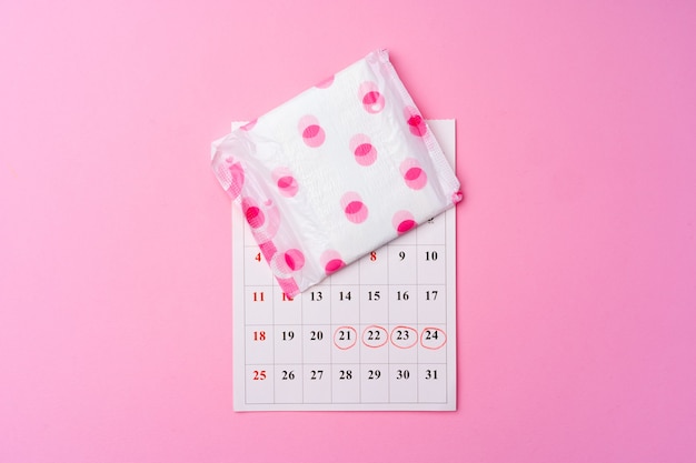 Página de calendario y almohadilla higiénica femenina en la vista superior de fondo rosa