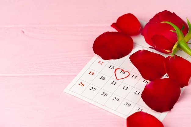 Foto página de calendario de febrero con rosa roja sobre mesa de madera rosa de cerca