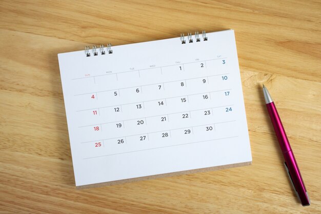 Página de calendario con lápiz sobre mesa de escritorio de madera