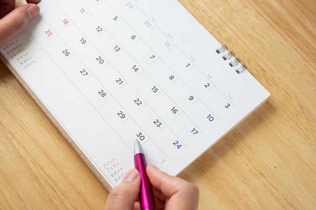 Página de calendario con mano femenina sosteniendo la pluma sobre la mesa de escritorio