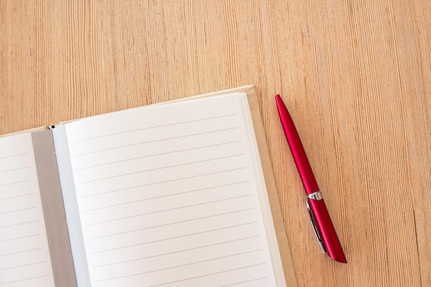 Página de cuaderno en blanco de escritorio de oficina y bolígrafo rojo sobre fondo de mesa de oficina de madera