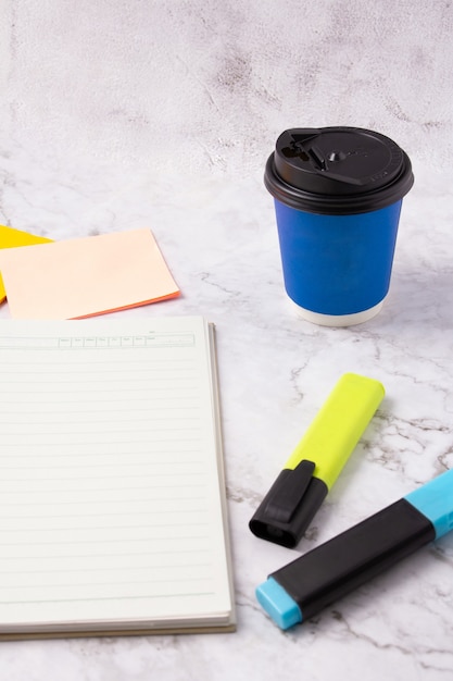 Página de cuaderno en blanco de libro abierto, rotulador azul, nota adhesiva y taza de café azul en la mesa de mármol blanco. escritorio de oficina de mármol. modelo. Fondo.