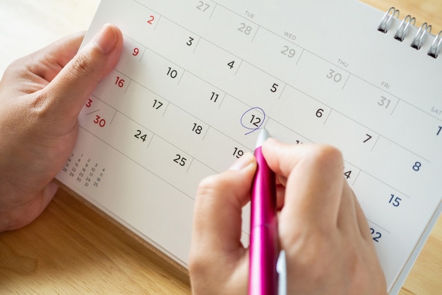 Foto página do calendário com uma mão feminina segurando uma caneta na mesa