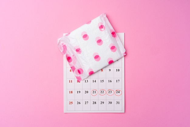 Foto página do calendário e almofada higiênica feminina na vista superior do fundo rosa