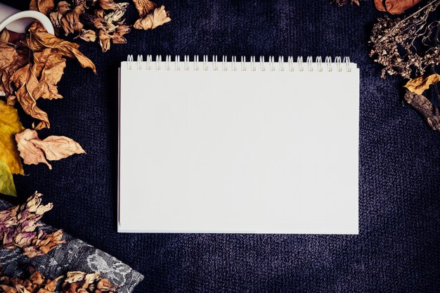 Página em branco caderno branco rodeada por folhas amarelas marrons secas e flores em azul escuro