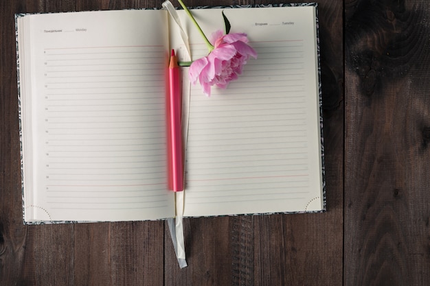 Página em branco do caderno e lápis, flor rosa na mesa de madeira